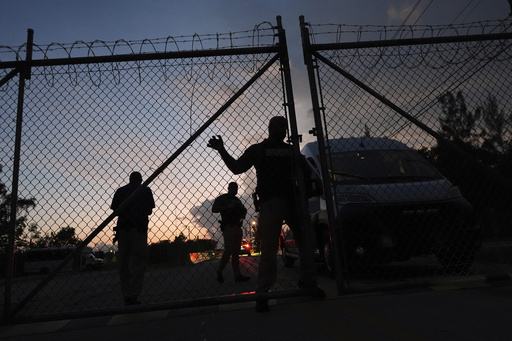 Krome Detention Center officers man an entrance gate as people hold a vigil outside to recognize those who have died in U.S. Immigration and Customs Enforcement custody, as well as those affected by mass deportations, Saturday, May 24, 2025, in Miami. (AP Photo/Rebecca Blackwell)