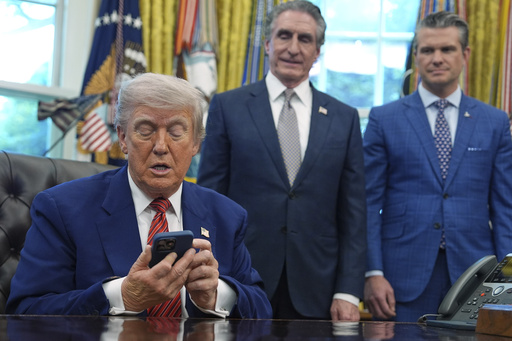 President Donald Trump silences his phone that rang twice as he was speaking to reporters after signing executive orders regarding nuclear energy in the Oval Office of the White House, Friday, May 23, 2025, in Washington, as Interior Secretary Doug Burgum and Defense Secretary Pete Hegseth watch. (AP Photo/Evan Vucci)