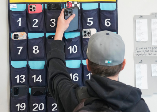 FILE - A ninth grader places his cellphone into a phone holder as he enters class at Delta High School, Friday, Feb. 23, 2024, in Delta, Utah. (AP Photo/Rick Bowmer, file)