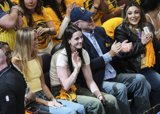 Caitlin Clark, center, waves from her seat during the first half of Game 6 of the Eastern Conference finals of the NBA basketball playoffs between the New York Knicks and the Indiana Pacers in Indianapolis, Saturday, May 31, 2025. (AP Photo/AJ Mast)
