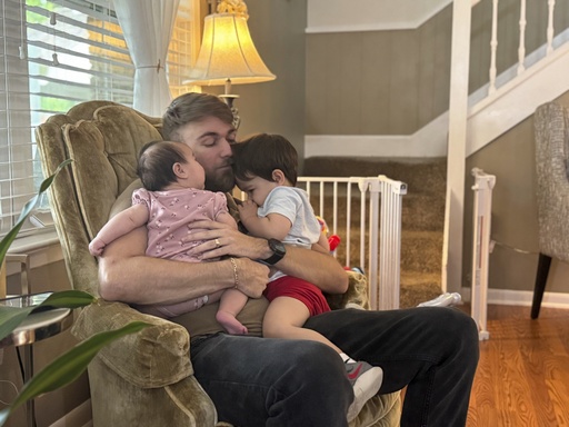 U.S. Marine Corps veteran Adrian Clouatre holds his 3-month-old daughter Lyn and his nearly two old son Noah at their home in Baton Rouge, La. on Tuesday, June 17, 2025. (AP Photo/Stephen Smith)