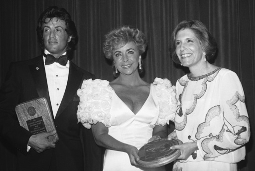 FILE - Wallis Annenberg, right, presents Elizabeth Taylor, center, and Sylvester Stallone with Devereux Foundation Awards at a ceremony, Thursday, July 12, 1984, Beverly Hills, Calif. (AP Photo/Nick Ut, file)