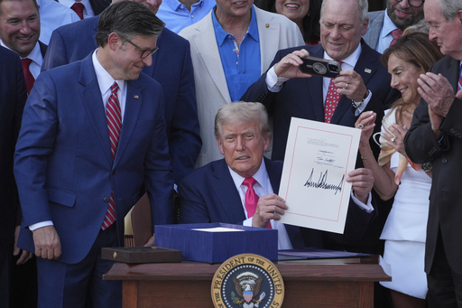 President Donald Trump holds his signed signature bill of tax breaks and spending cuts at the White House, Friday, July 4, 2025, in Washington, as House Speaker Mike Johnson of La., left, watches and Rep. Steve Scalise, R-La., takes a photo. (AP Photo/Evan Vucci)