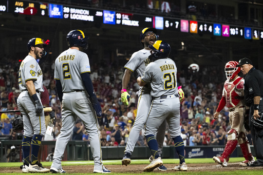 Milwaukee Brewers Andruw Monasterio, center, and Caleb Durbin (21) celebrate after Monasterio's home run in extra innings of a baseball game against the Cincinnati Reds, Saturday, Aug. 16, 2025, in Cincinnati. (AP Photo/Michael Swensen)