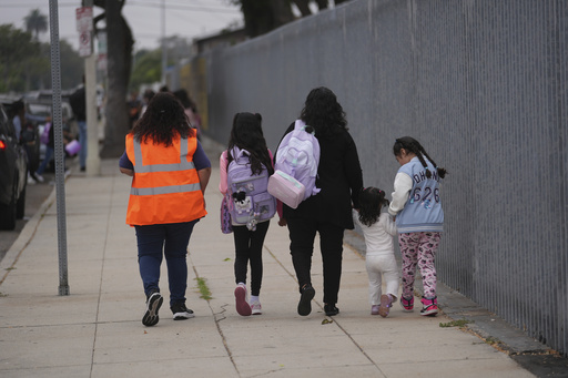 Students and family members are escorted into school on the first day of school Thursday, Aug. 14, 2025, in Los Angeles. (AP Photo/Marcio Jose Sanchez)