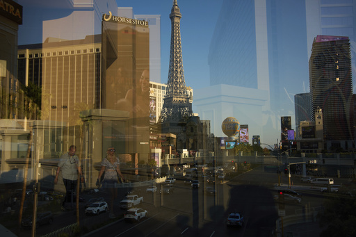 Reflected in a glass window, people walk across a pedestrian bridge along the Las Vegas Strip, Friday, Aug. 8, 2025, in Las Vegas. (AP Photo/John Locher)