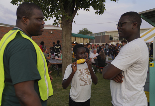 Samy Yawo, center, eats sweet corn at the St. Jude Catholic Church's Sweet Corn Festival as his father, Billy Yawo, right, talks with, Roger Atchou, left, a father of two from Togo, on Saturday, Aug. 9, 2025, in Cedar Rapids, Iowa. (AP Photo/Jessie Wardarski)