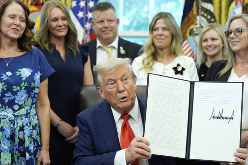 President Donald Trump, surrounded by family members of soldiers killed in Afghanistan at the attack at Abbey Gate, holds up a signed proclamation honoring the fourth anniversary of the attack, in the Oval Office of the White House, Monday, Aug. 25, 2025, in Washington. (AP Photo/Alex Brandon)