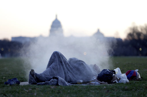 FILE - The U.S. Capitol building gives backdrop to a homeless man resting on a steam vent on the National Mall, Dec. 18, 2019, on Capitol Hill in Washington. (AP Photo/Julio Cortez, File)