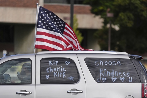 A vehicle marked with messages written on its windows in tribute to Turning Point USA CEO and co-founder Charlie Kirk and carrying an American flag, drive past at Utah Valley University, Saturday, Sept. 13, 2025, in Orem, Utah. (AP Photo/Lindsey Wasson)