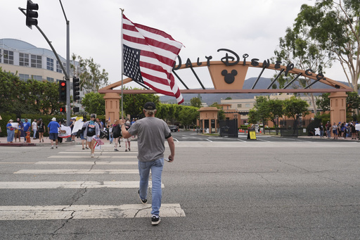 A U.S. flag is carried across a street in front of a demonstration in response to the suspension of Jimmy Kimmel's late-night show outside of Walt Disney Studios in Burbank, Calif., on Thursday, Sept. 18, 2025. (AP Photo/Jae C. Hong)