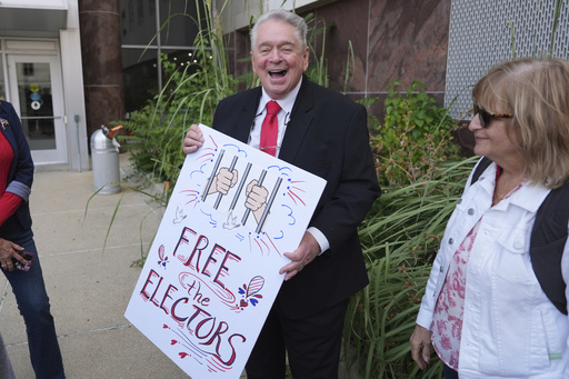 Clifford Frost holds a sign after a Michigan judge dismissed the criminal cases against 15 people accused of acting falsely as electors for President Donald Trump in the 2020 election Tuesday, Sept. 9, 2025 in Lansing, Mich. (AP Photo/Paul Sancya)