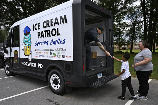 Norwich Police School Resource Officer Bob McKinney hands an ice cream to Alby Little as his mother Sylvia Little, right, looks on in Norwich, Conn., on Thursday, Aug. 21, 2025. (AP Photo/Jessica Hill)