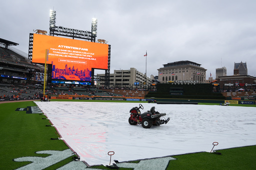 A tarp covers the field as rain falls while a message is seen on a video board alerting fans the start of Game 3 of baseball's American League Division Series between the Detroit Tigers and the Seattle Mariners will be delayed Tuesday, Oct. 7, 2025, in Detroit. (AP Photo/Ryan Sun)