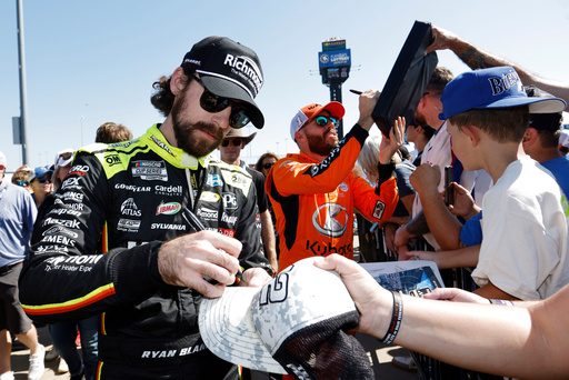 CORRECTS TO ROSS CHASTAIN NOT BUBBA WALLACE - Ryan Blaney, left, and Ross Chastain, center, give autographs before a NASCAR Cup Series auto race at Kansas Speedway in Kansas City, Kan., Sunday, Sept. 28, 2025. (AP Photo/Colin E. Braley)