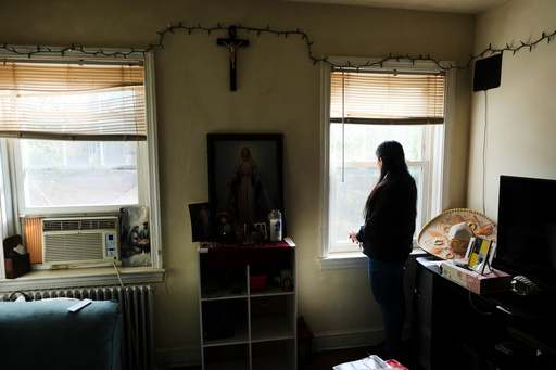 A parishioner of the Shrine of the Sacred Heart, whose husband was detained by immigration agents, looks out her home's window as she poses for a portrait in Washington, Friday, Oct. 10, 2025. (AP Photo/Luis Andres Henao)
