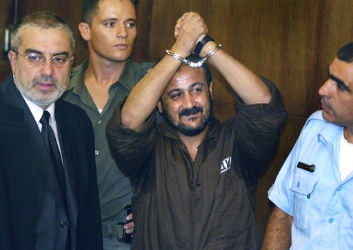 FILE - Marwan Barghouti, center, raises his handcuffed hands in the air on the opening day of his trial in Tel Aviv, Israel, Aug. 14, 2002. (AP Photo/Brennan Linsley, File)