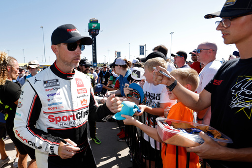 Denny Hamlin, left, gives autographs before a NASCAR Cup Series auto race at Kansas Speedway in Kansas City, Kan., Sunday, Sept. 28, 2025. (AP Photo/Colin E. Braley)