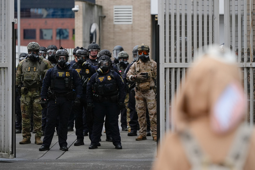 Law enforcement officers watch as the gates close at a U.S. Immigration and Customs Enforcement facility as people protest outside on Saturday, Oct. 11, 2025, in Portland, Ore. (AP Photo/Jenny Kane)