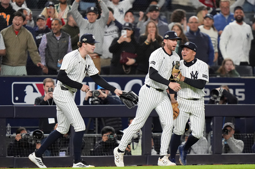 New York Yankees third base Ryan McMahon, center, is congratulated by pitcher Cam Schlittler, left, and shortstop Anthony Volpe after making a catch over the Boston Red Sox dugout during the eighth inning of Game 3 of an American League wild-card baseball playoff series, Thursday, Oct. 2, 2025, in New York. (AP Photo/Frank Franklin II)