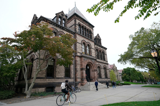 FILE - Passers-by walk and ride along a path on the campus of Brown University, in Providence, R.I., Monday, Oct. 12, 2020. (AP Photo/Steven Senne, File)