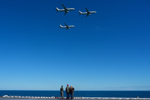 President Donald Trump and first lady Melania Trump watch a flight of P-8A Poseidon aircraft during a naval sea power demonstration, part of the Navy's 250th anniversary celebration, aboard the USS George H.W. Bush aircraft carrier in the Atlantic Ocean off the coast of Norfolk, Va., Sunday, Oct. 5, 2025. (AP Photo/Alex Brandon)