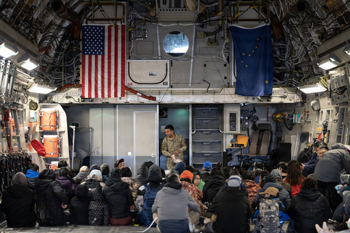 In this photo provided by the Alaska National Guard, Alaska Air National Guard Staff Sgt. Angel Reyes distributes hearing protection to passengers while evacuating Alaskans displaced in the aftermath of Typhoon Halong out of Bethel, Alaska, Wednesday, Oct. 15, 2025. (Alaska National Guard via AP)