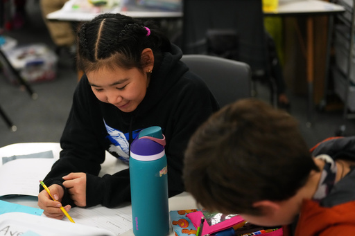 Rayann Martin, a 10-year-old displaced from the village of Kipnuk by ex-Typhoon Halong, left, talks with new classmate Lilly Loewen, 10, right, as they work in the Yup'ik language at College Gate Elementary, Thursday, Oct. 30, 2025, in Anchorage, Alaska. (AP Photo/Lindsey Wasson)