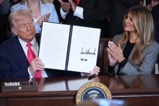 President Donald Trump displays an signed executive order as first lady Melania Trump watches during an event on foster care in the East Room of the at the White House, Thursday, Nov. 13, 2025, in Washington. (AP Photo/Evan Vucci)